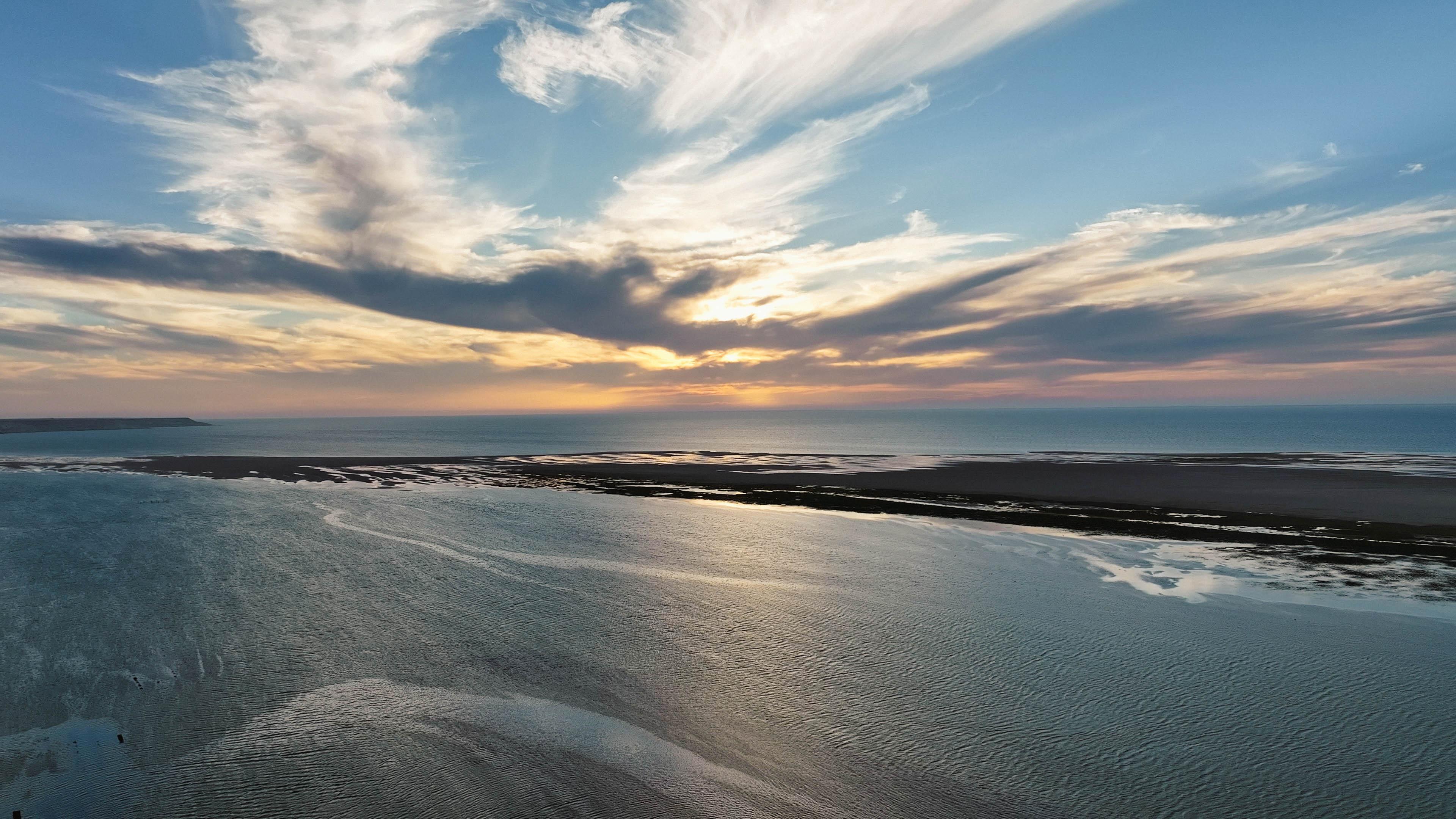Sunset over the Dakhla lagoon with flat turquoise water stretching toward the Sahara desert, a world-class destination for kitesurfing, wingfoil and surf.