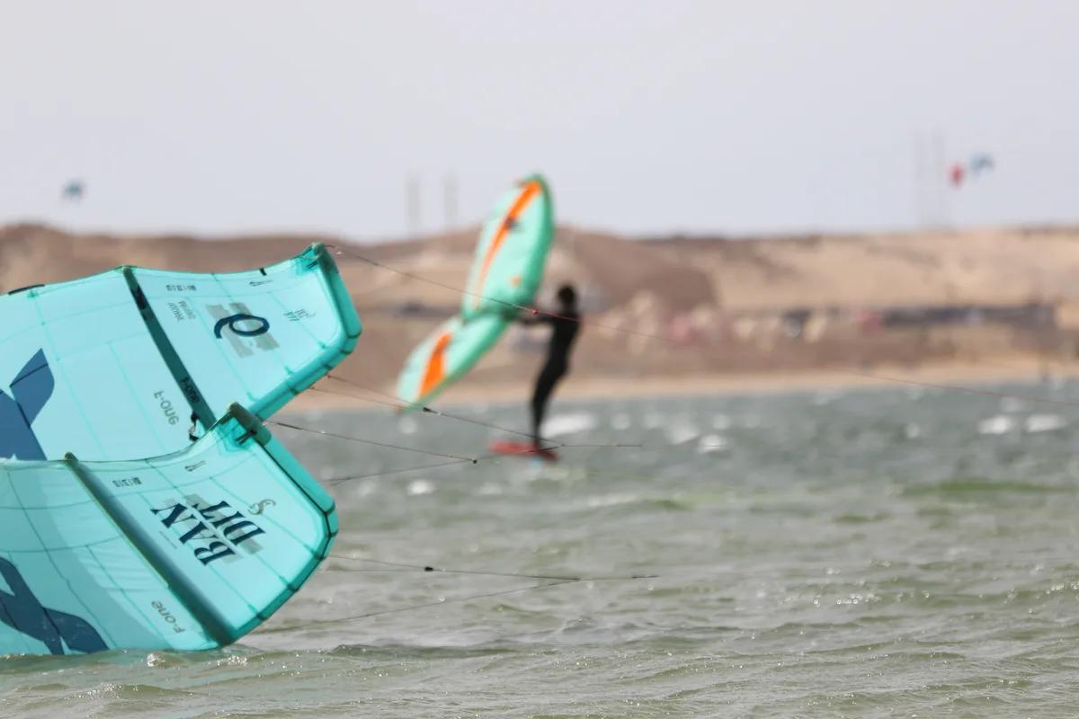 Bluboarding wingfoil client riding past a kite on the turquoise water of the Dakhla lagoon on a sunny day with rental equipment.