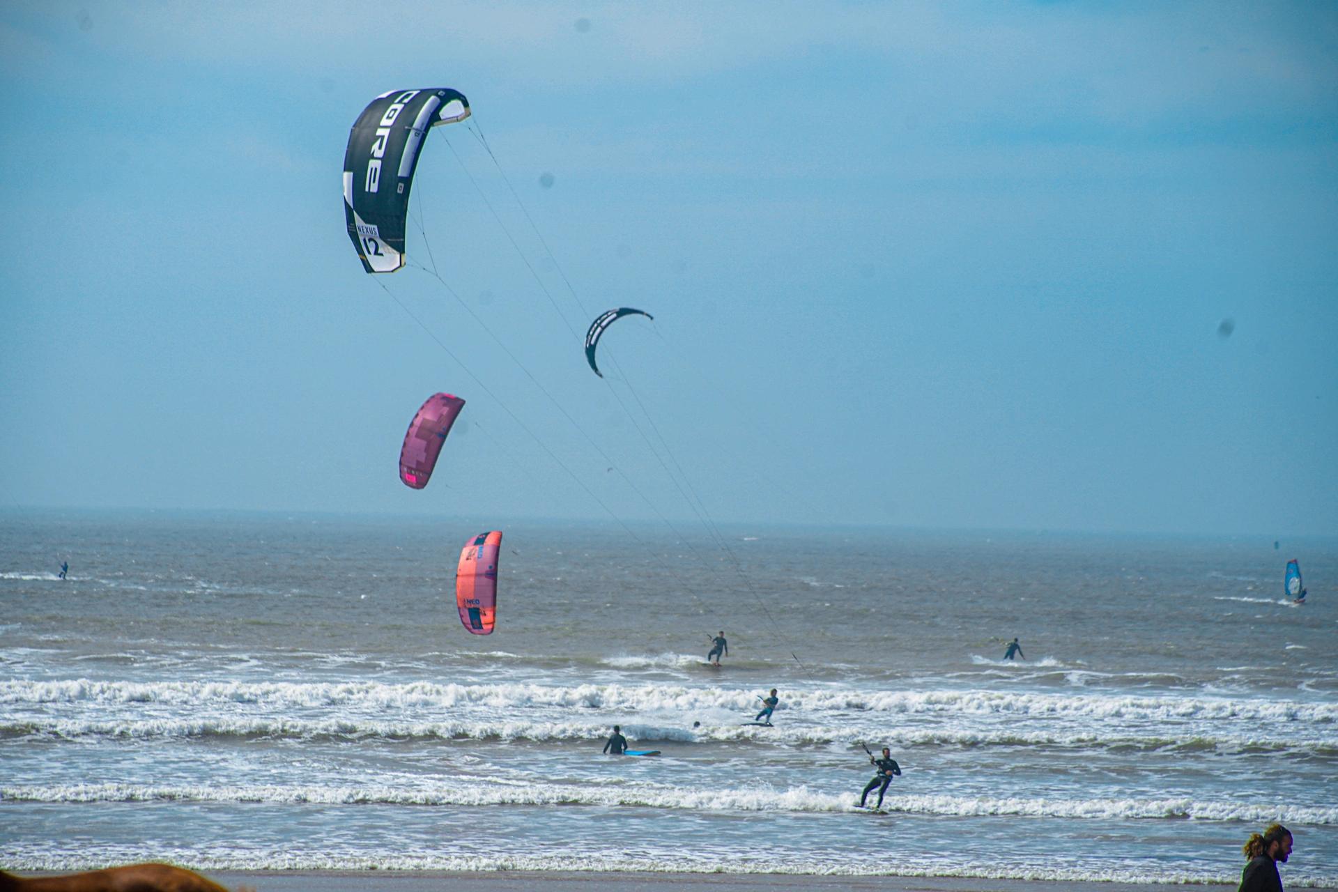 Bluboarding clients kitesurfing on a windy day with choppy chocolate-colored water on the main beach of Essaouira.