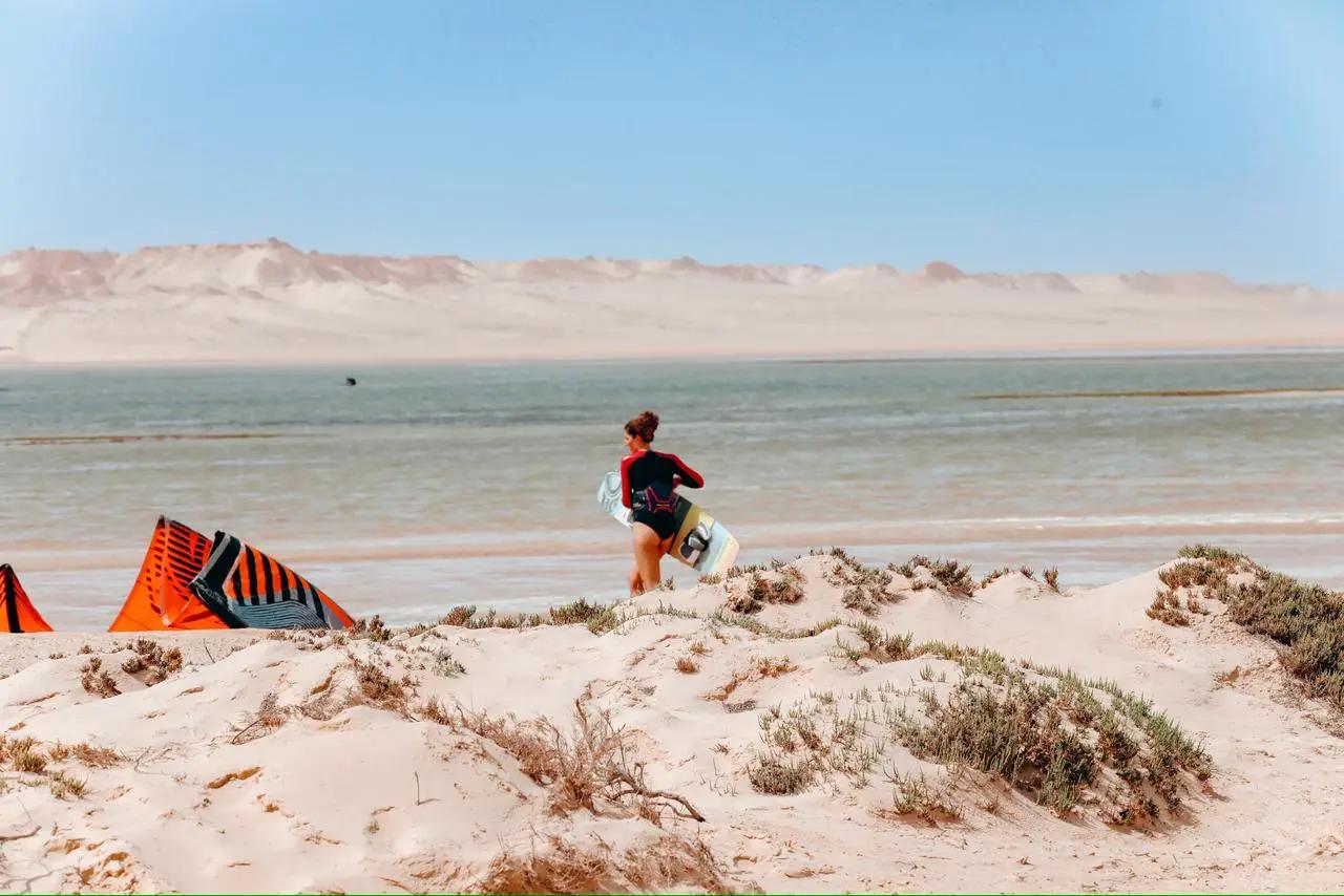 Kitesurf student holding her board on the beach at Secret Spot in Dakhla, Morocco, preparing for a session in calm conditions