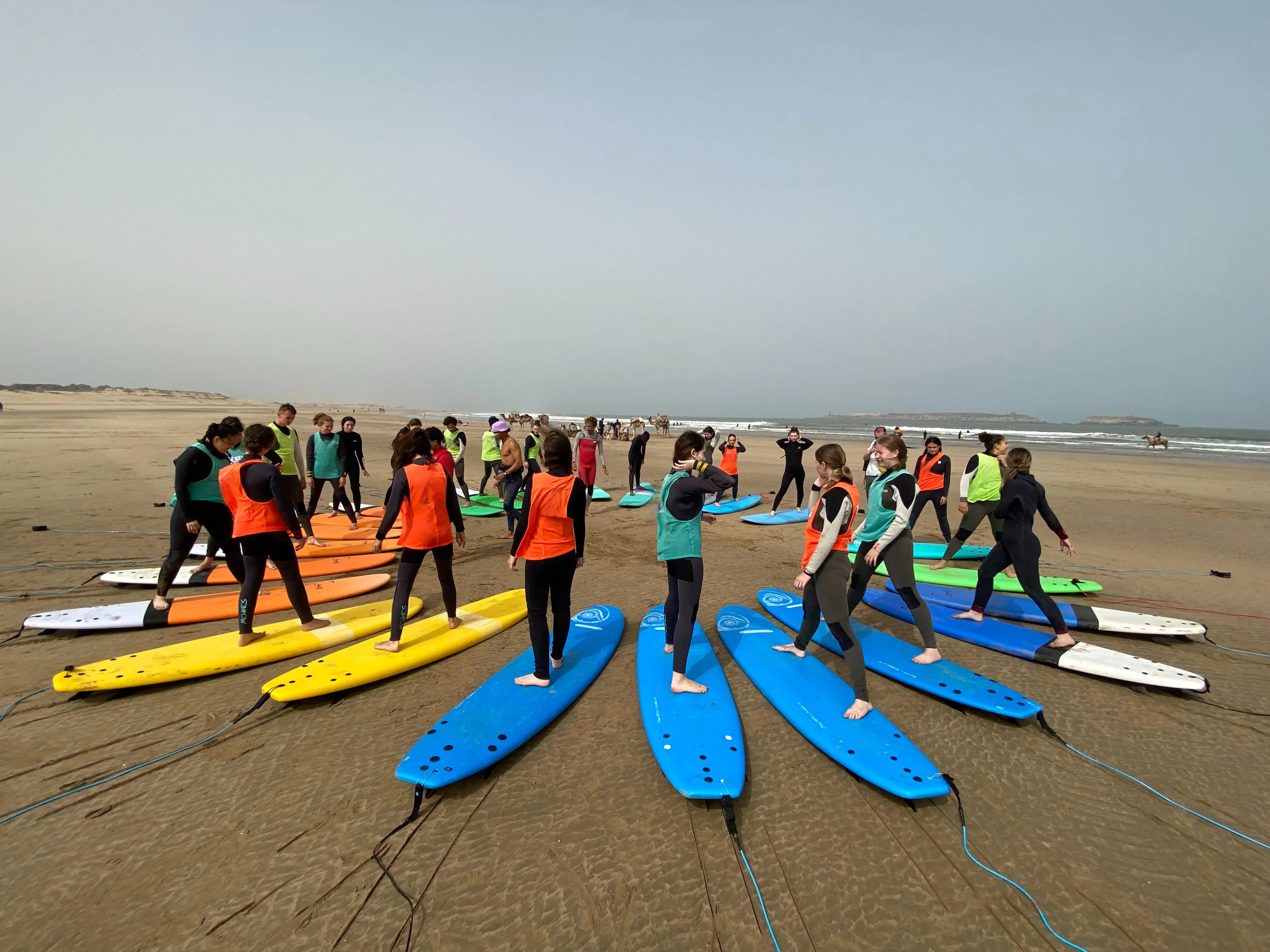 Bluboarding surf instructor explaining the correct stance to avoid nose-diving to a group of students on the beach near Dakhla during a group surf lesson.