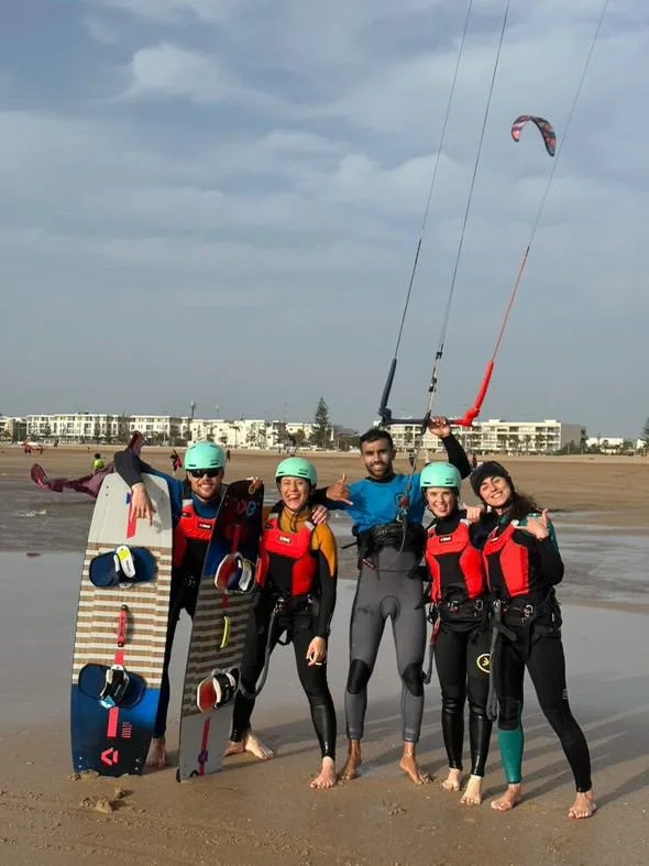 Happy group of Bluboarding kitesurf clients posing with their instructor on the beach of Essaouira for a souvenir photo after a group lesson.