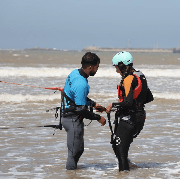 Bluboarding kitesurf instructor helping a client hook the kite before her waterstart on the main beach of Essaouira.