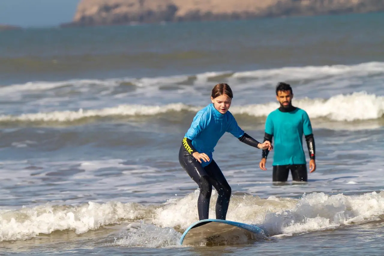 Young Bluboarding client catching a wave on the main beach of Essaouira while her surf instructor watches from behind during a private lesson.