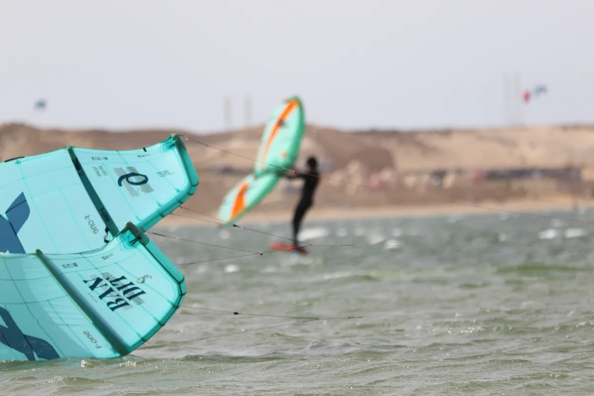 Bluboarding wingfoil rental client riding past a kitesurfer using rental equipment on the Dakhla lagoon, showcasing the combo rental option.
